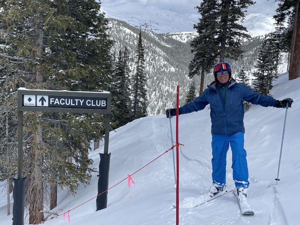 Glenn Mueller, on skis, in front of a trail called "Faculty Club"