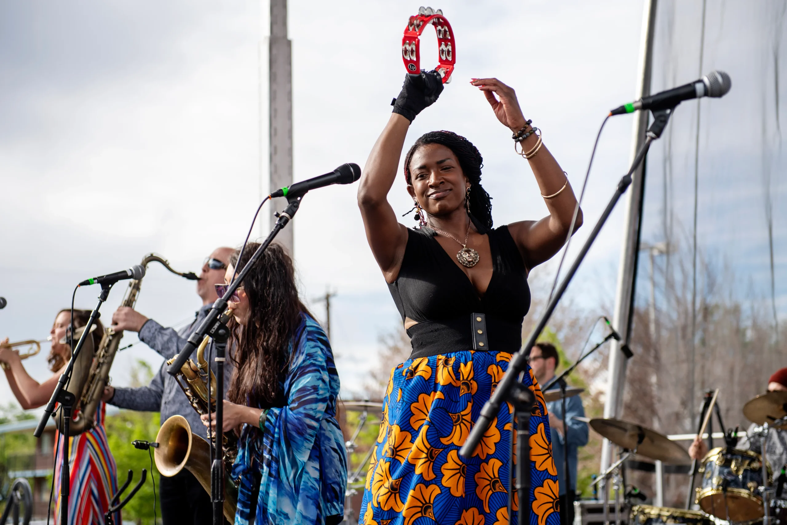 A woman on a stage dancing with a tambourine while two saxophonists play
