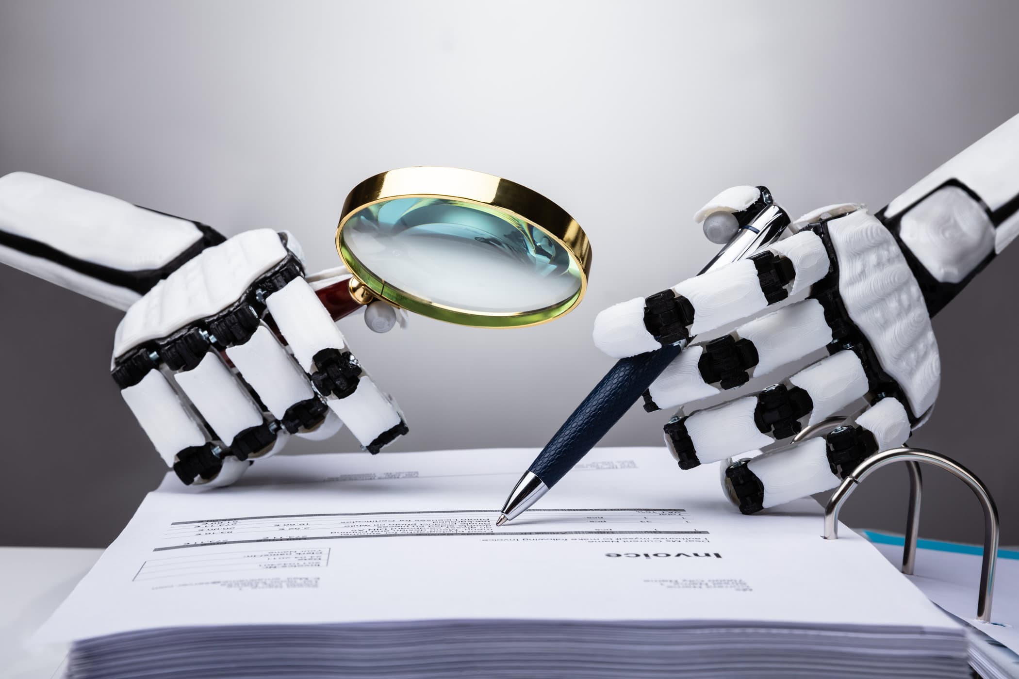 Robotic hands holding a magnifying glass and pen over an audit form