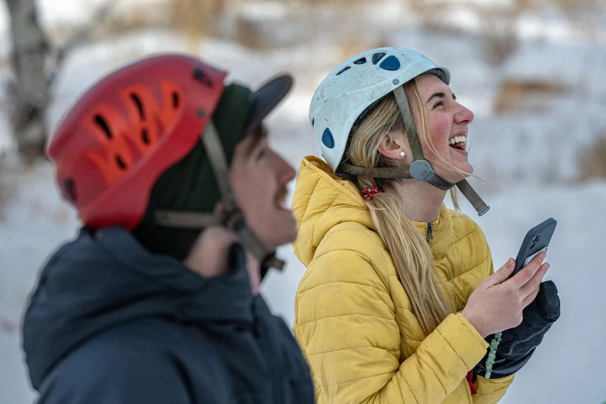 Students smiling in climbing helmets and winter coats in a snowy environment