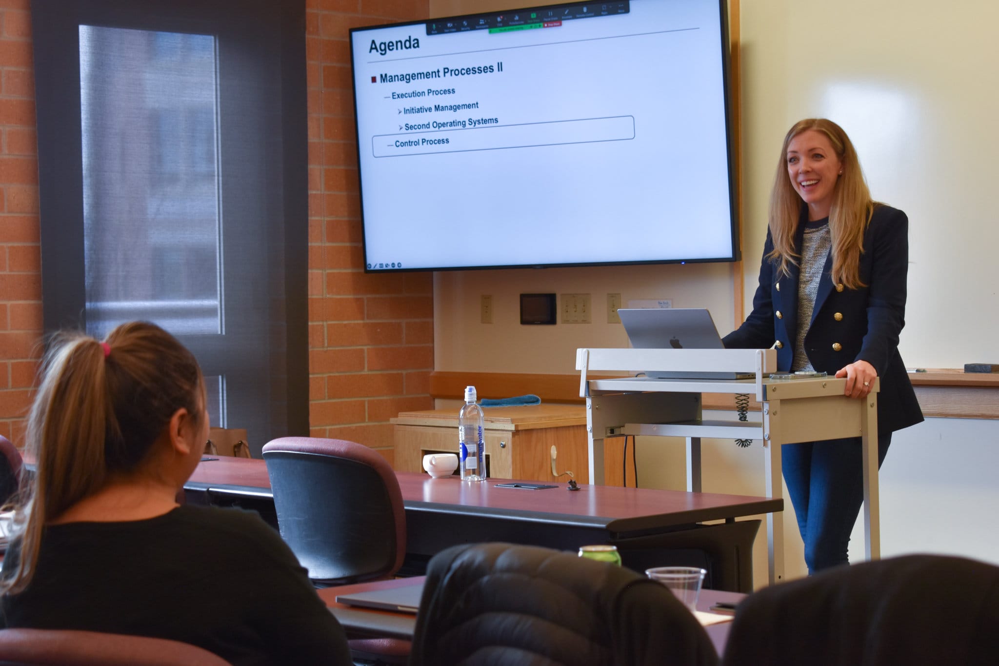 Belinda Oakley stands at a lectern in front of a PowerPoint screen