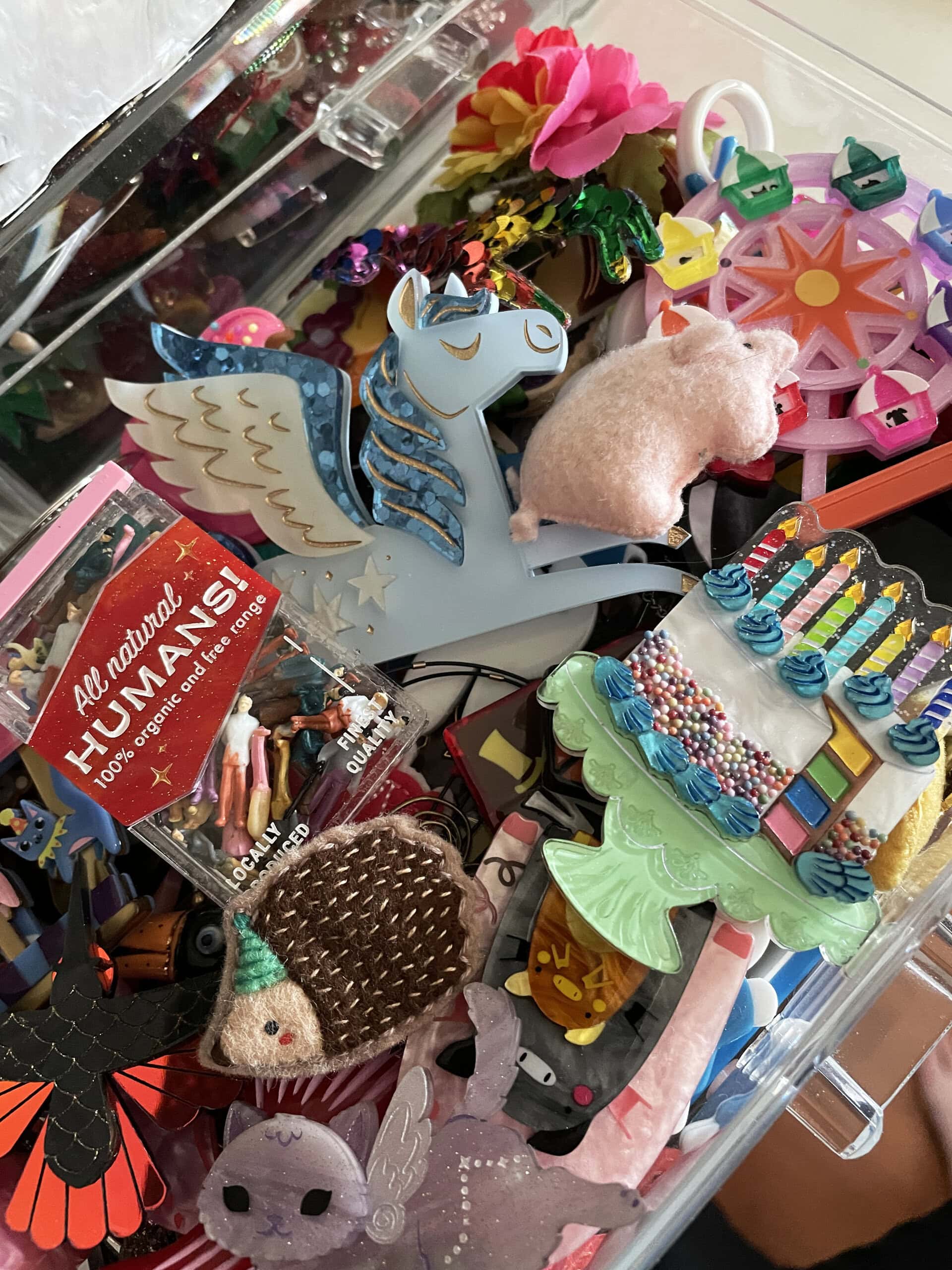 A drawer of Brooke Goodell's brooches, including a flying unicorn, a birthday cake, a hedgehog in a birthday hat, and more