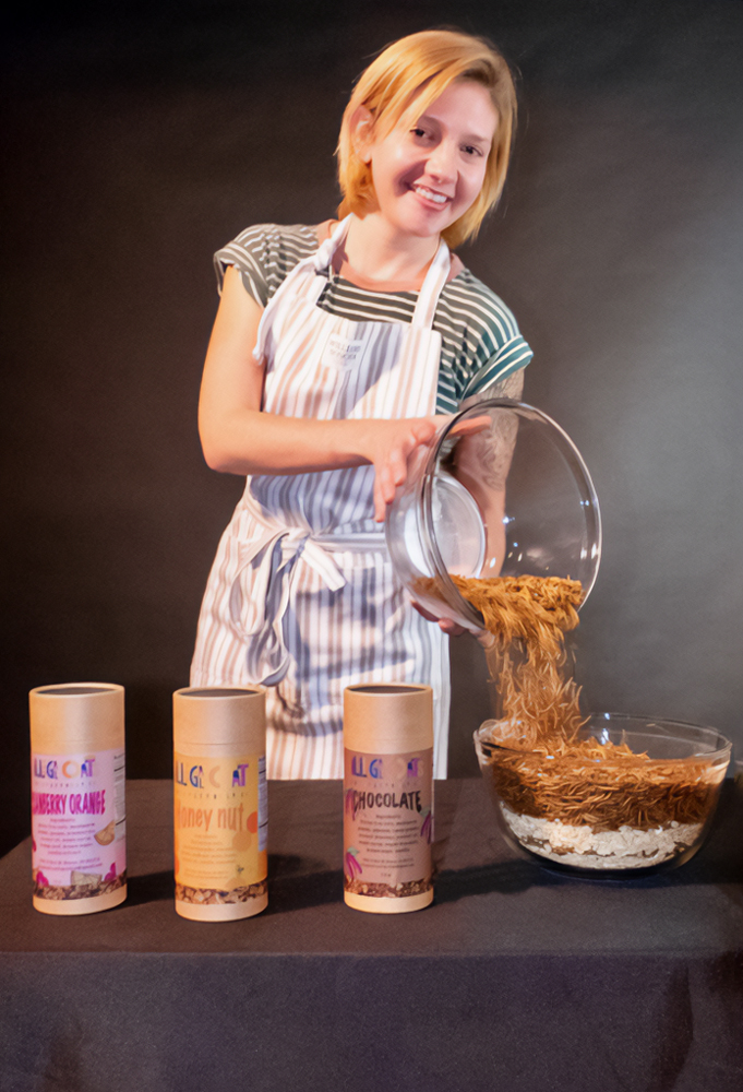 Clare Whetzel pours a bowl of her Illegal Oats granola behind a display of three of her products.