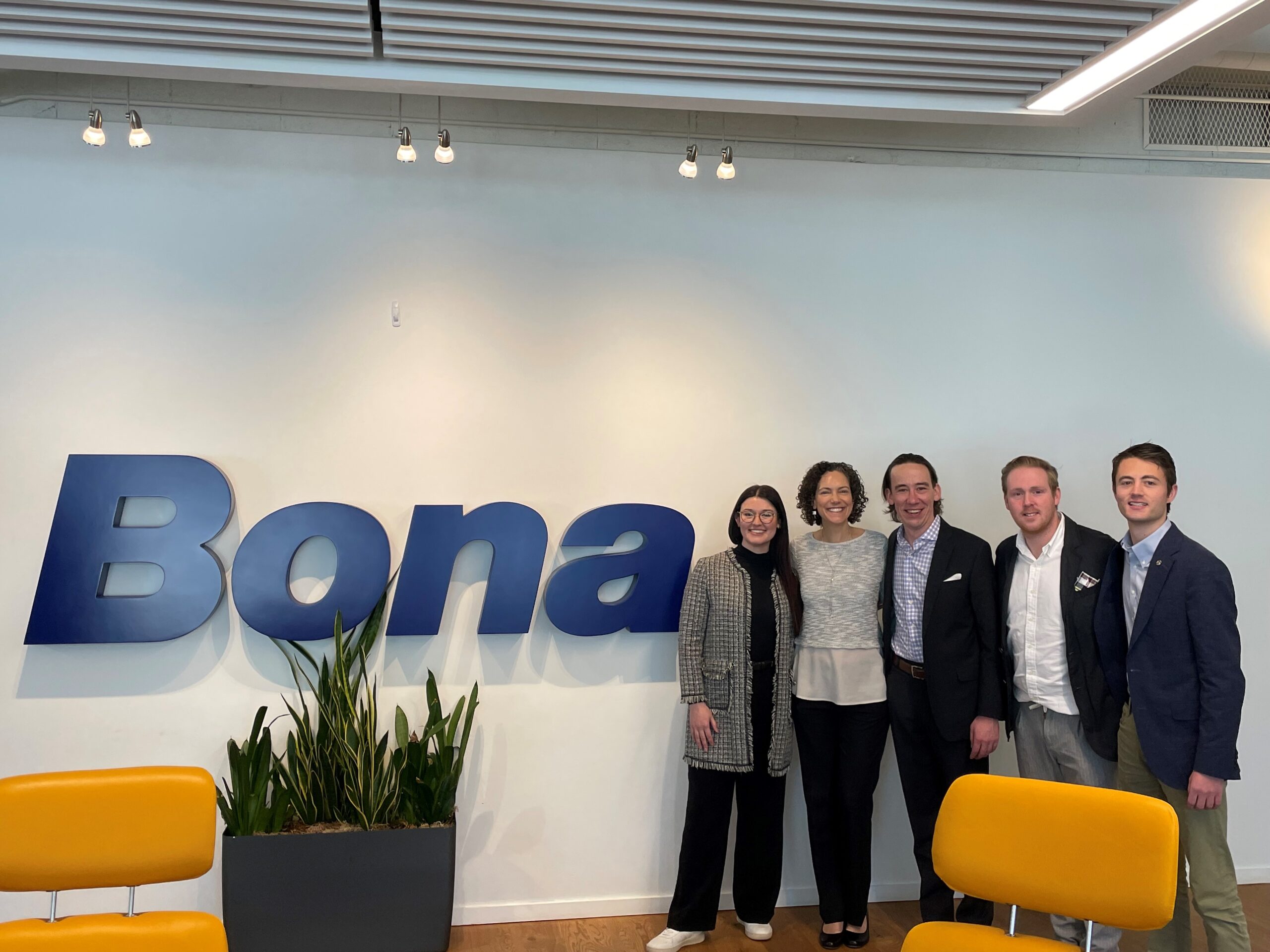 A group of five students in professional attire next to a Bona sign in a conference room