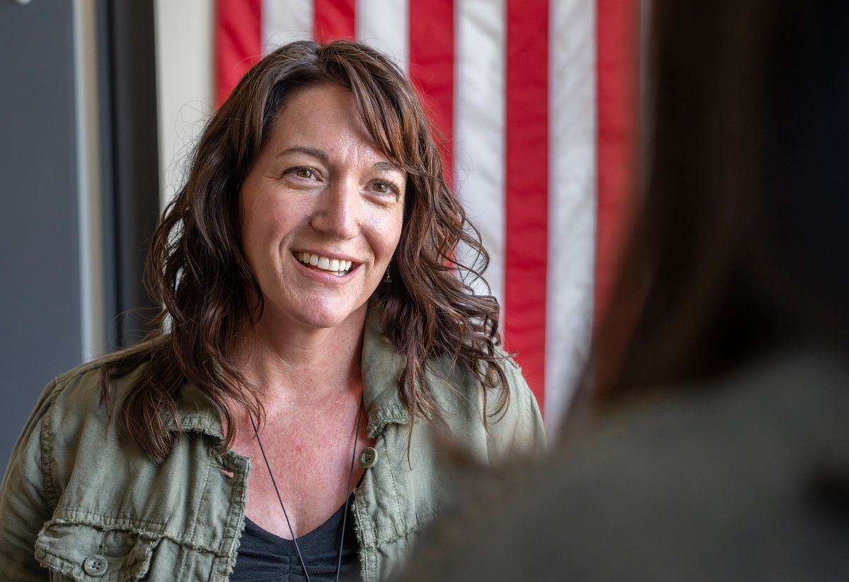 A woman in front of an American flag talking with someone else