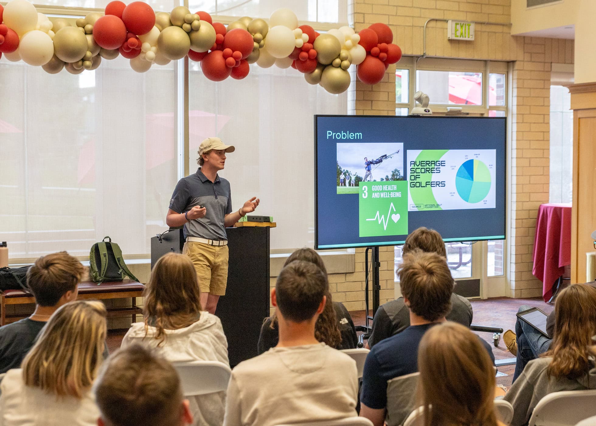 A student in golf clothing pitching an idea in front of a screen displaying pie chart with average scores of golfers