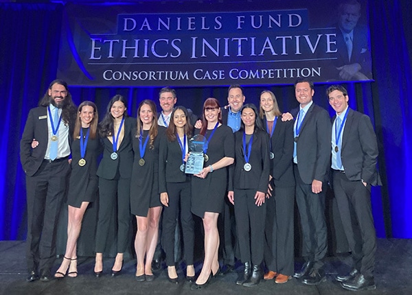 Students in business attire pose with a trophy and medals around their necks.
