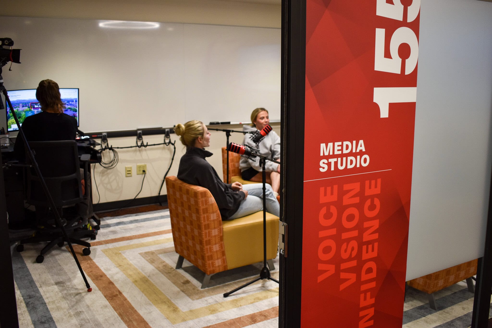 Students in chairs behind podcast mics