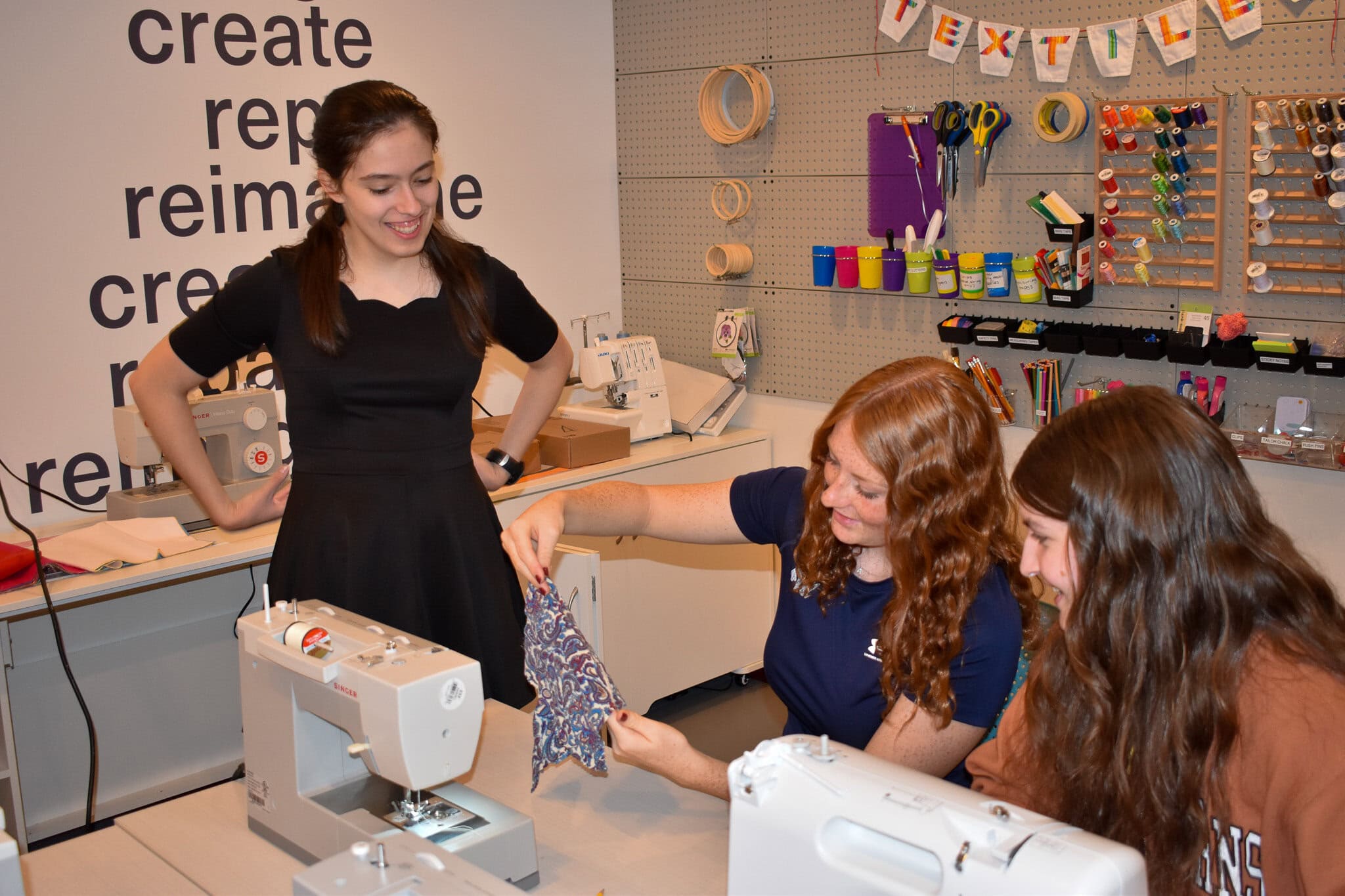 Students sitting at sewing machines in front of spools of thread.