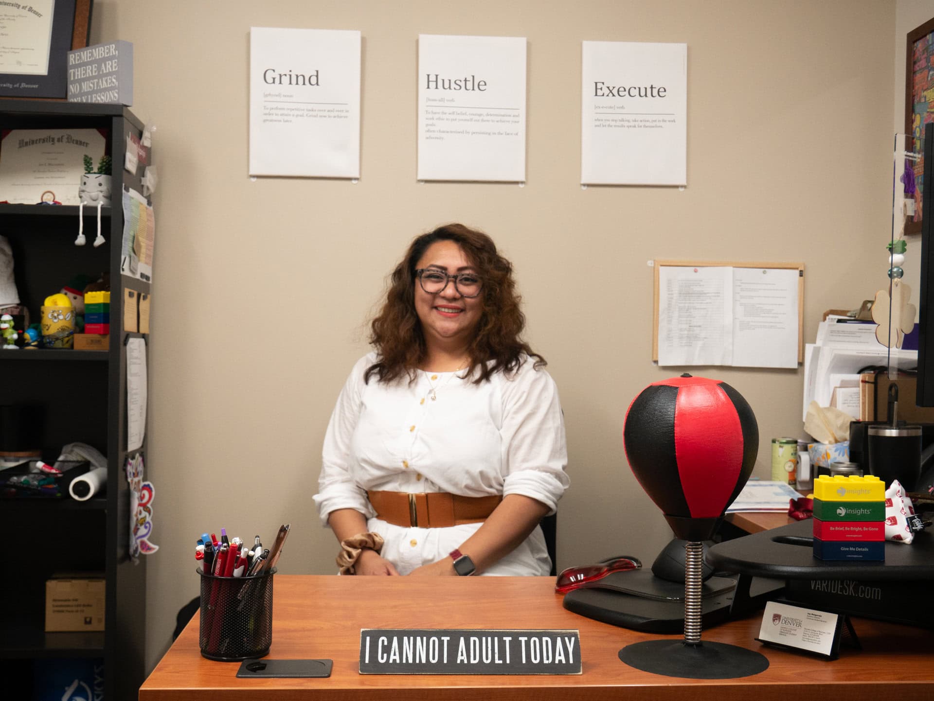 Joy Melgarejo sitting in her office, beneath signs that say "Grind" "Hustle" and "Execute." A punching bag is to her left.