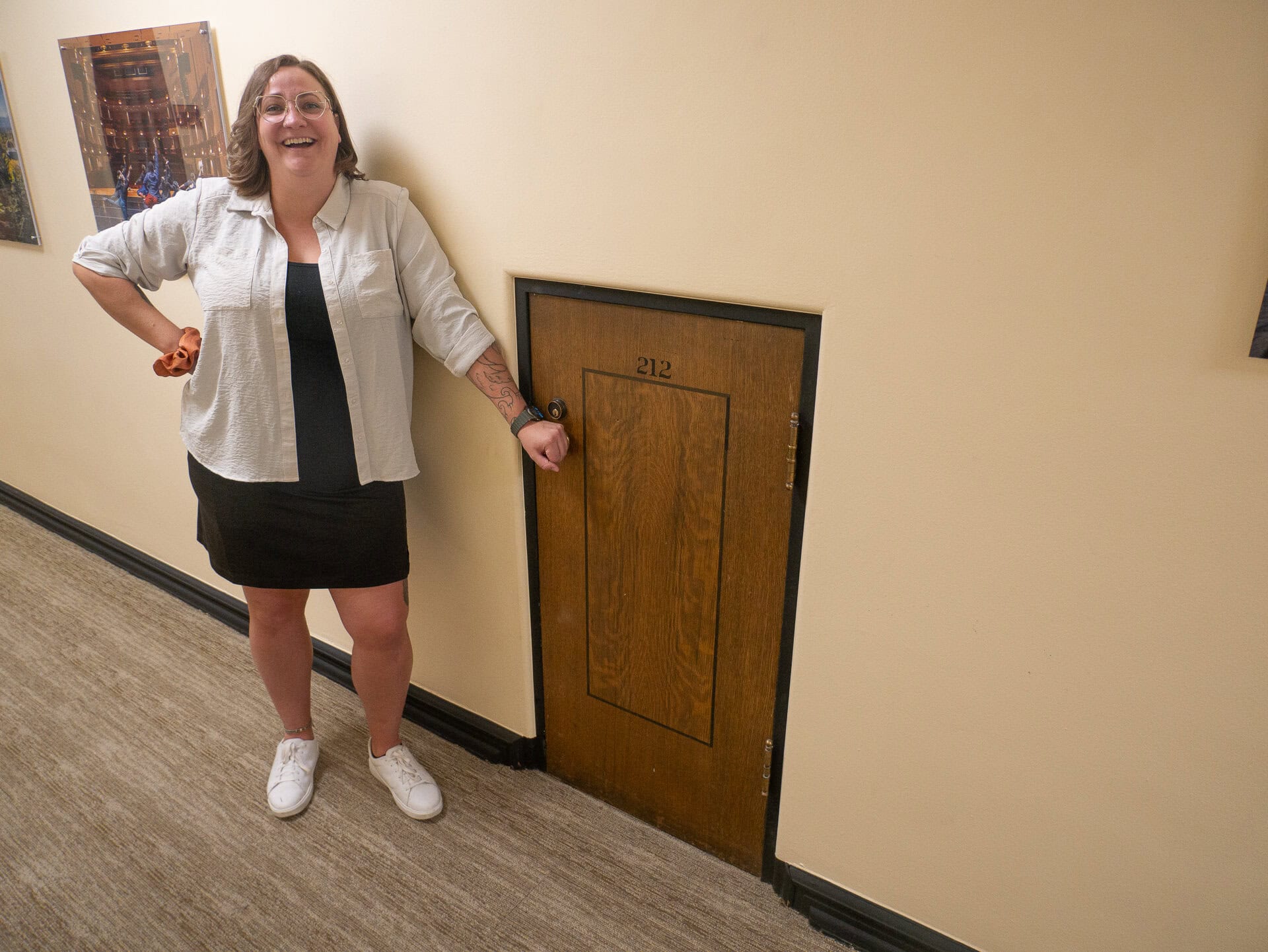 Lexi standing with her hand on the knob of a tiny door on campus.