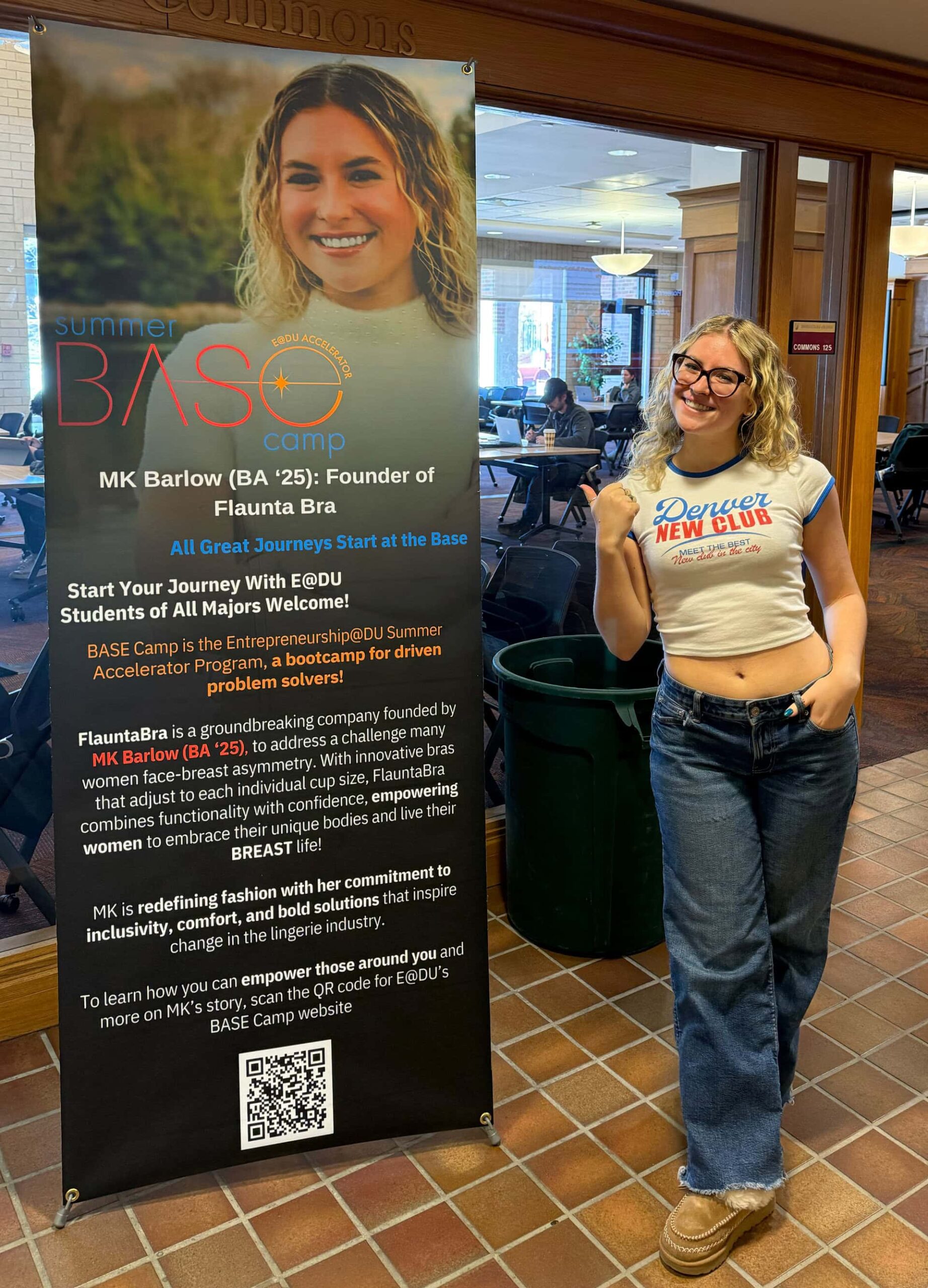 MK Barlow posing in front of a promotional poster for Entrepreneurship@DU with her face on it