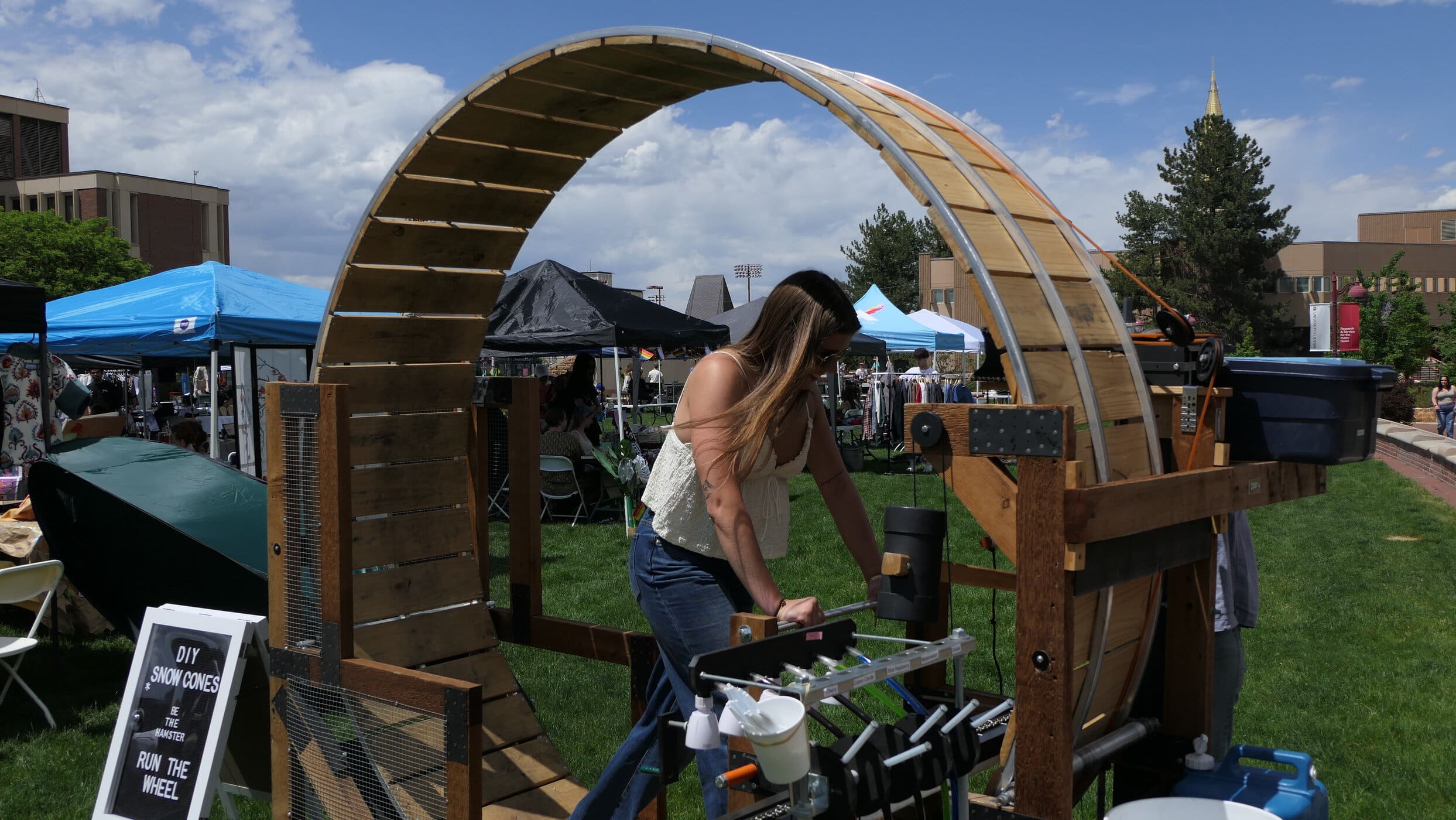 A student running in a wooden hamster wheel at a DIY Snow Cone station on Carnegie Green
