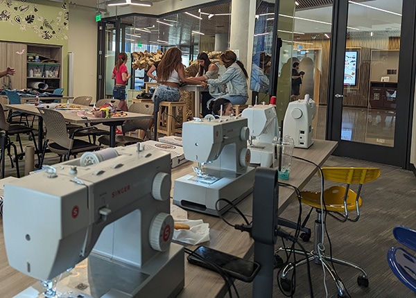 Sewing machines in the foreground, students around a table in the background