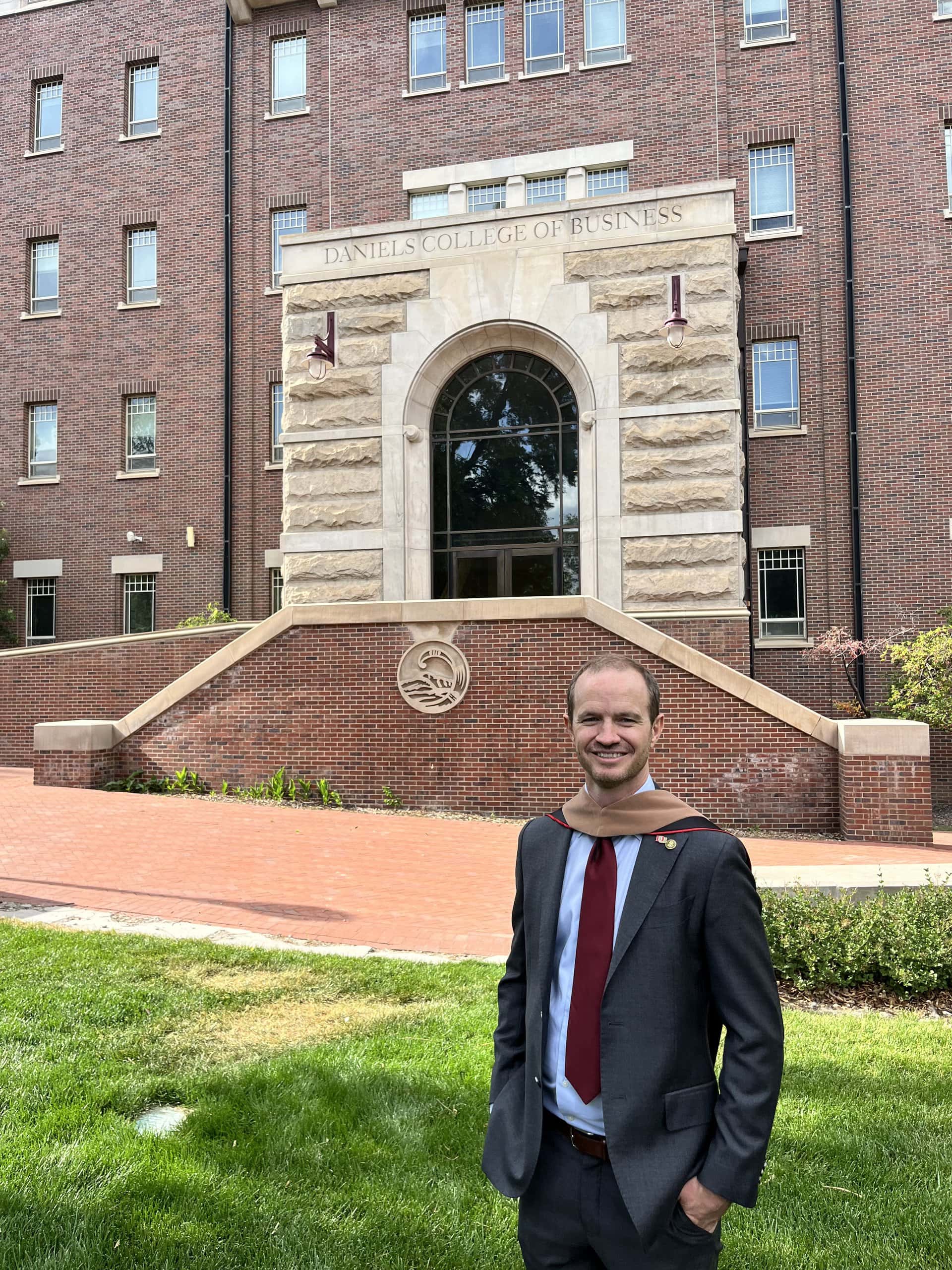 Steve Delp stands in a suit and graduation hood in front of the Daniels College of Business