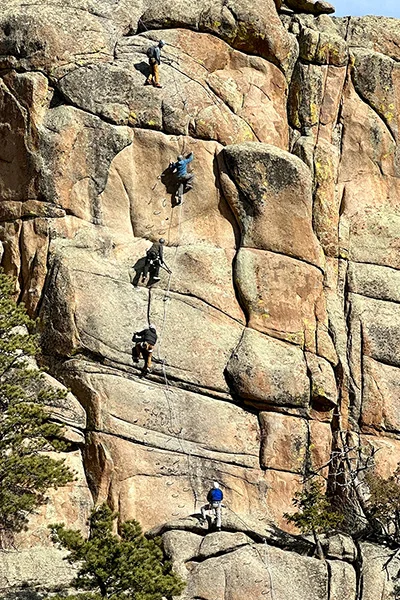 Climbers scaling a rock face standing on iron rungs, harnessed with cables