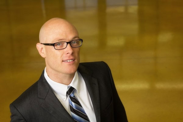 Adam Booker, new faculty member at the Daniels College of Business, shown in a professional portrait for a faculty announcement.