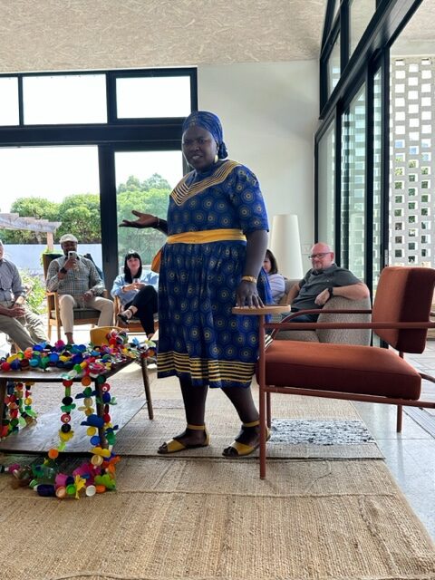 Woman gestures with her left hand while speaking to students inside a home