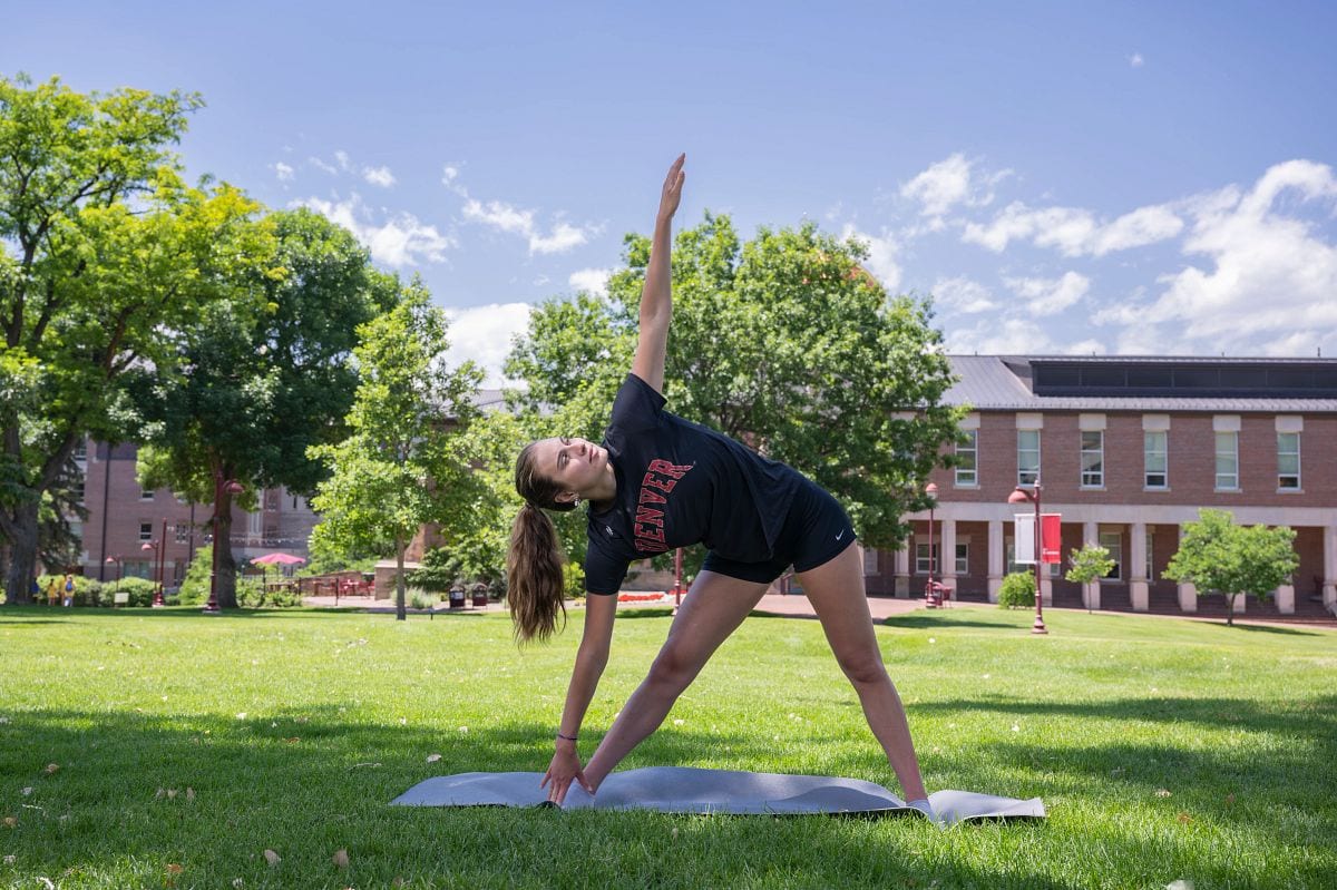 Student doing yoga on a mat on the campus green